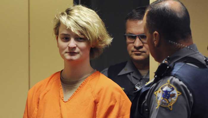 A photo of the accused, Denali Brehmer, in the courtroom, with police officers present.