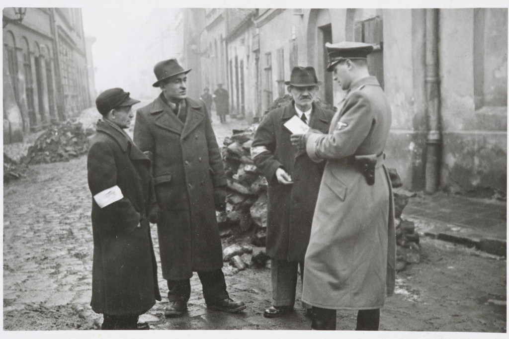 A German policeman checks the identification papers of Jewish people in the Krakow ghetto. Poland. Circa 1941. A German policeman checks the identification papers of Jewish people in the Krakow ghetto. Poland. Circa 1941.