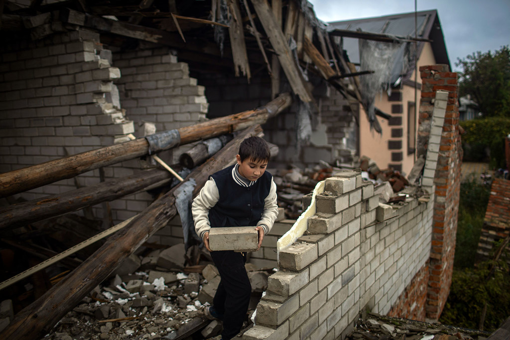 A nine-year-old boy helps his mother clear rubble from their heavily damaged home. A nine-year-old boy helps his mother clear rubble from their heavily damaged home.