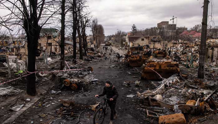A war-torn Ukrainian road, a citizen passes by on a bicycle.