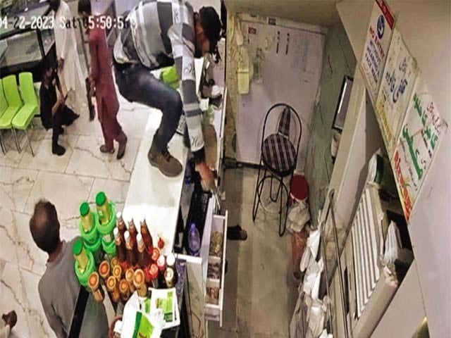 In Korangi, a dacoit is climbing over the cash counter of a sweet shop to rob.  Photo: Express