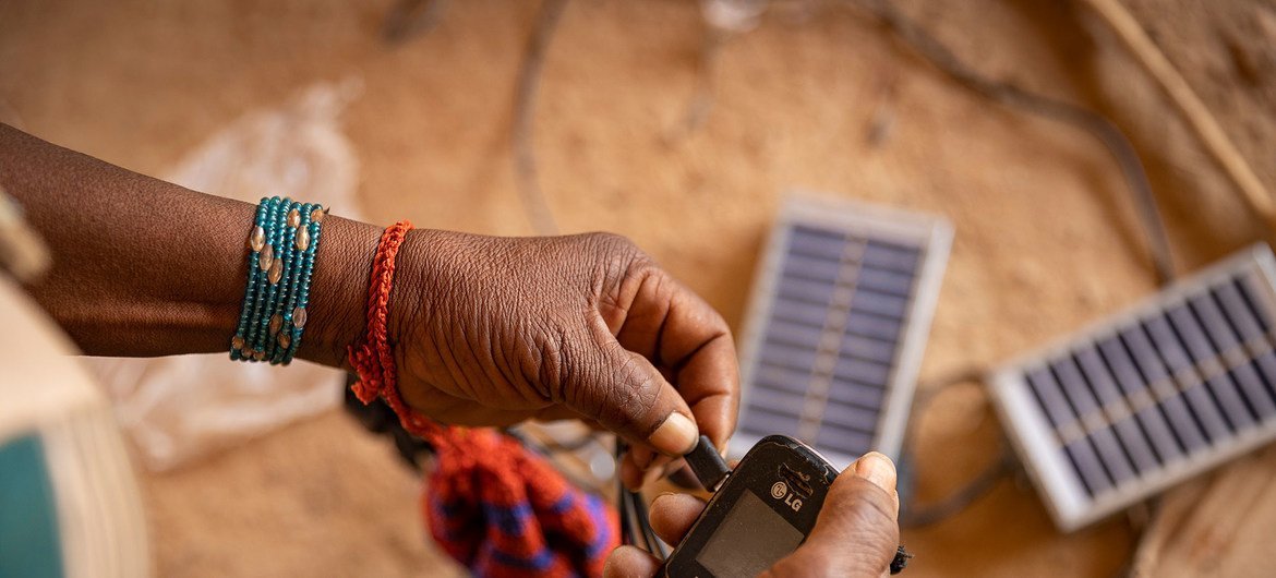 A woman uses solar energy to charge her cell phone in a displaced persons camp in Burkina Faso.