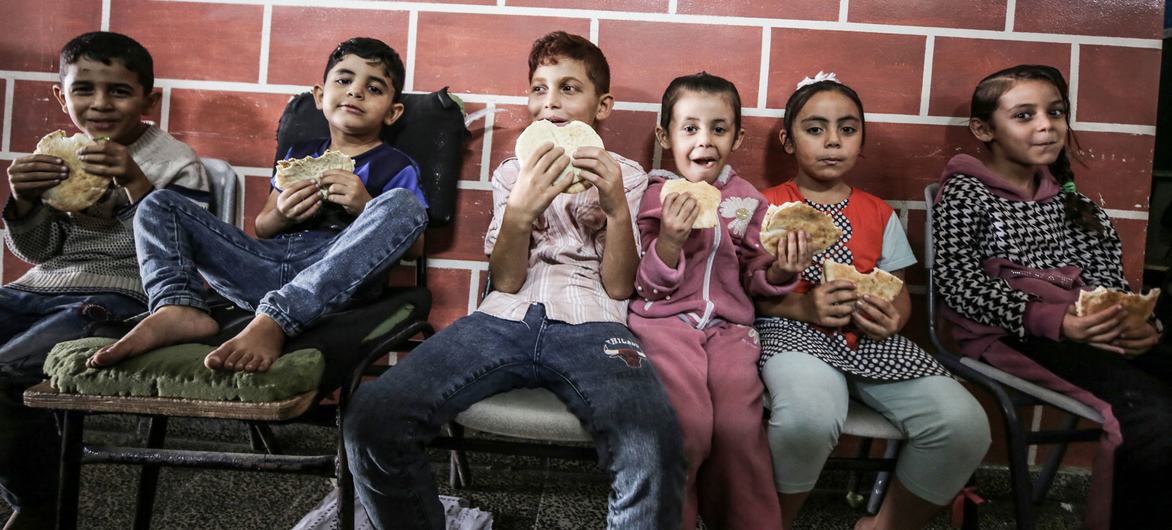 Children from families sheltering at an UNRWA school in Gaza eat bread distributed by the World Food Programme (WFP). Children from families sheltering at an UNRWA school in Gaza eat bread distributed by the World Food Programme (WFP).